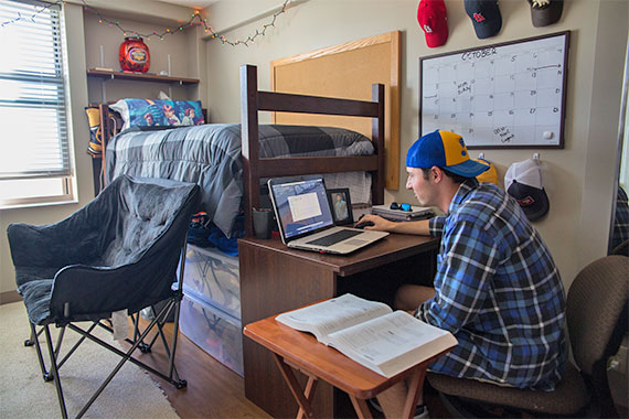 Male student working on laptop in residence hall room