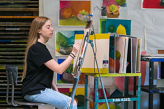 Student painting at easel in art studio classroom