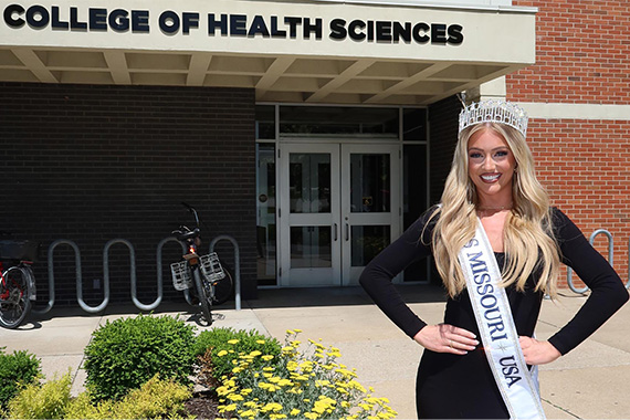 Woman in tiara and sash in front of building