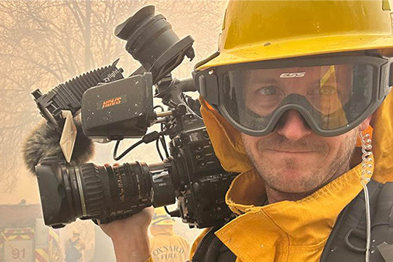 Man in fire-protective gear holding a film camera