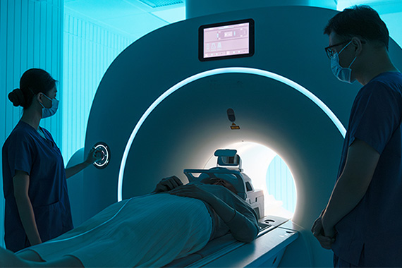 A patient in an MRI machine as two technicians stand beside the machine