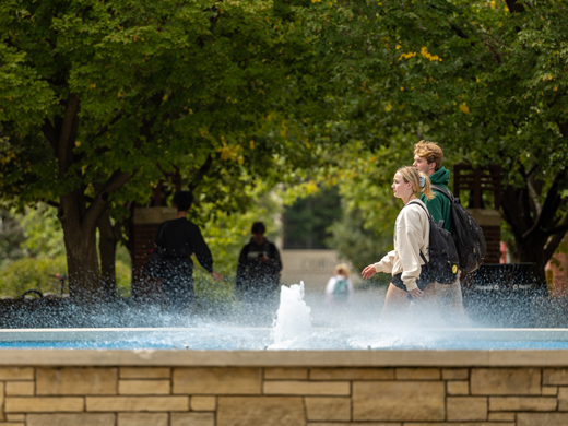 Students walking behind a fountain