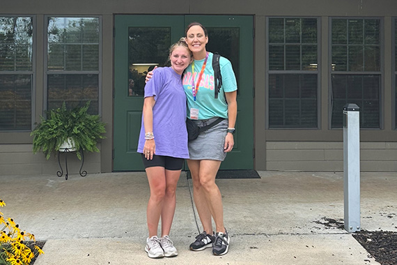 Two people in front of a summer camp building entrance
