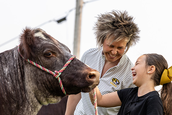 Woman talking to a young child who is laughing while petting a cow