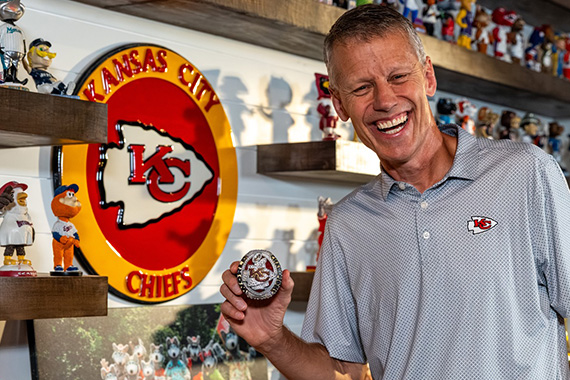 Man holding a large Super Bowl ring in front of shelves of sports collectibles