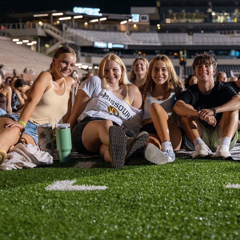 Students sitting on Faurot Field and smiling