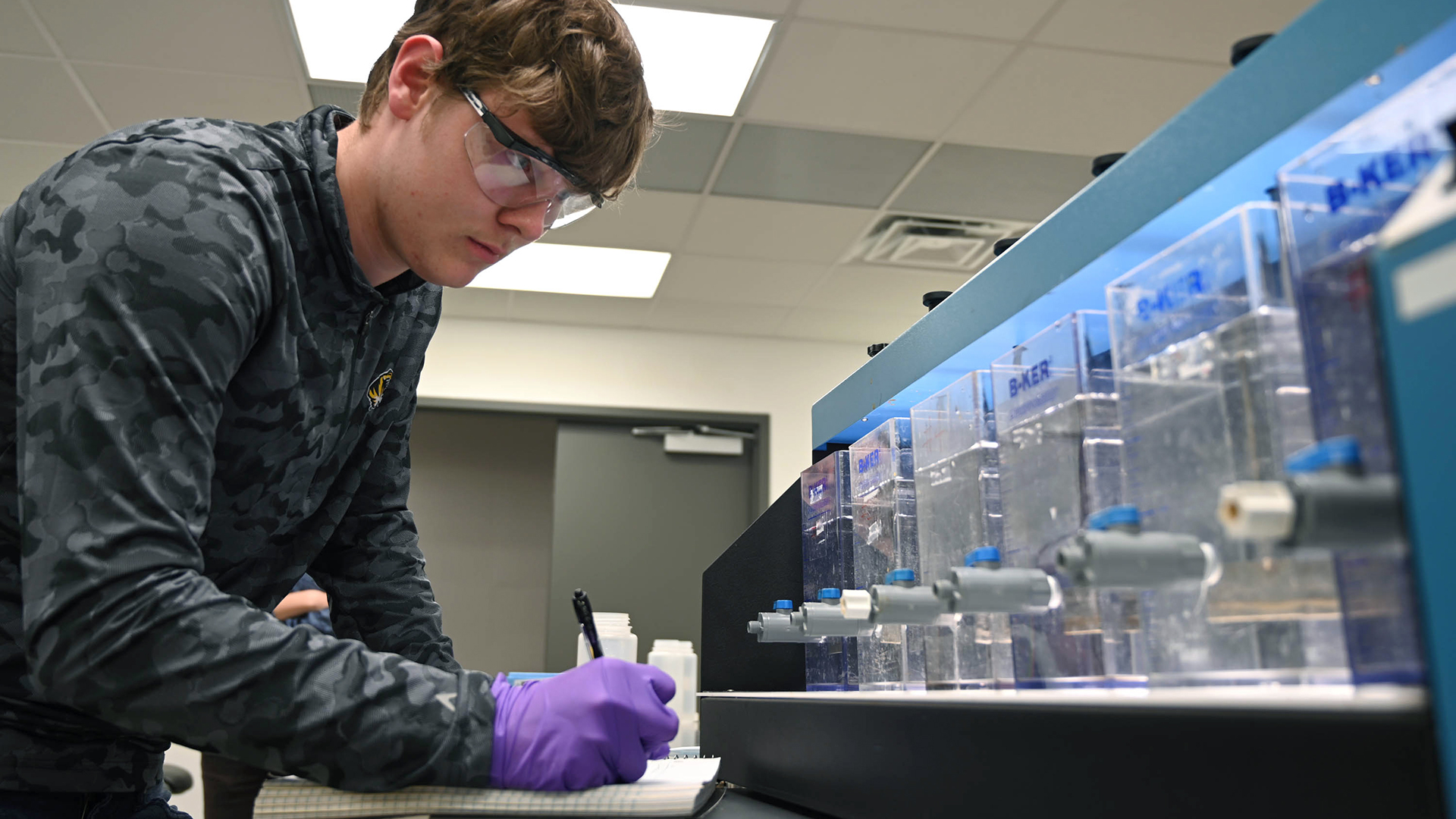A Mizzou student looking at various water samples and writing notes in a notebook