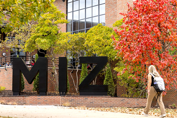 Student walking by a statue of the letters M-I-Z